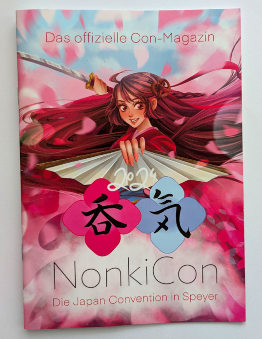 Cover of the convention guidebook of NonkiCon 2024. The mascot Nonki-Chan ist holding a fan