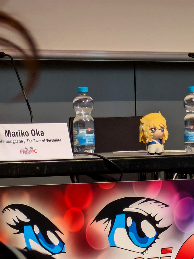 photo taken before the start of the Mappa panels showing the place Mariko Oka would soon sit. A cute Oscar plush is sitting on the table