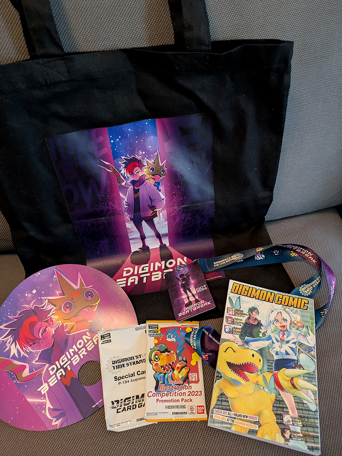 photo of the Digimon goodie bag every guest got at the panel: A black Digimon Beatbreak tote bag, a Digimon manga and special Digimon Trading cards. Also in the photos: goodies from the Bandai Namco booth